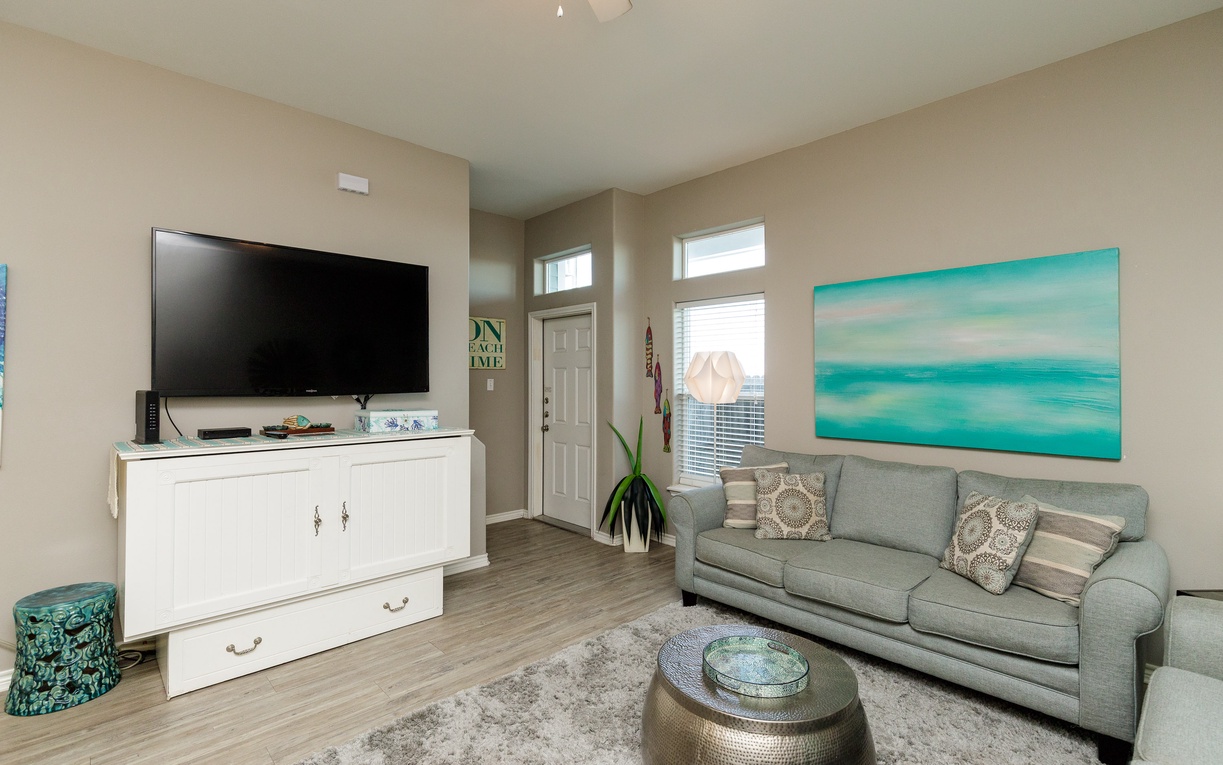 Relax in your coastal-themed living room where ocean artwork and soft gray furnishings create the perfect space for evening entertainment.