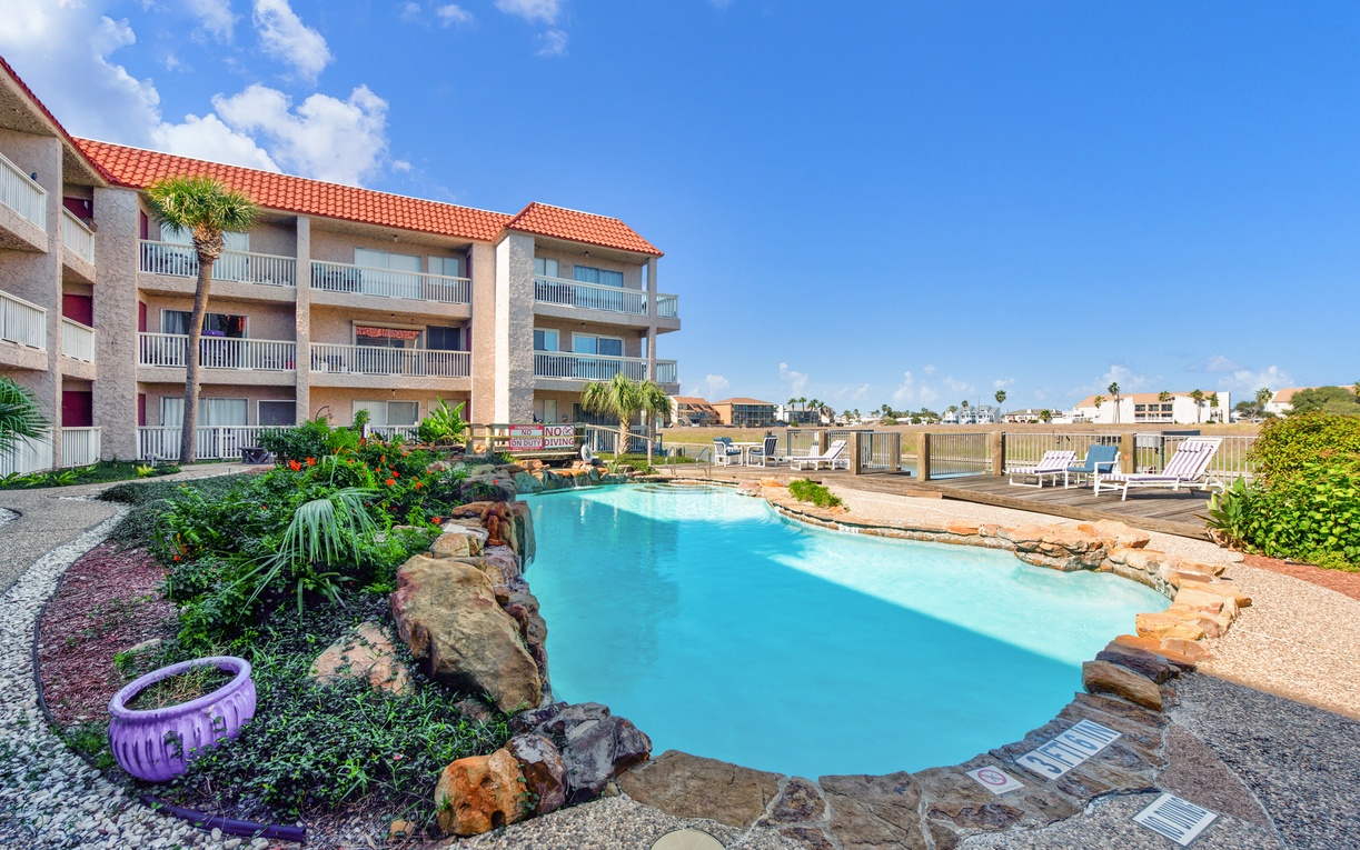 Crystal-clear pool surrounded by tropical landscaping creates your perfect outdoor escape beneath bright blue skies.