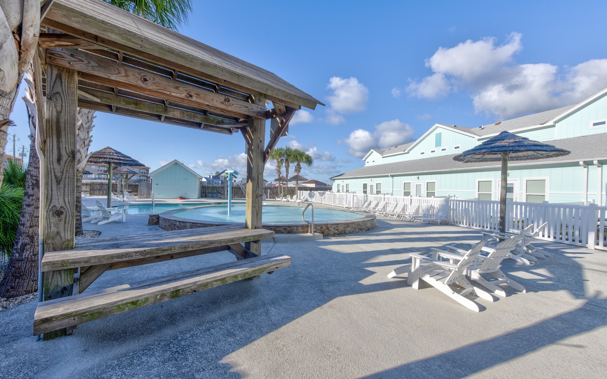 Beachside resort community featuring swimming pool, wooden pavilion, and colorful vacation homes under sunny skies.