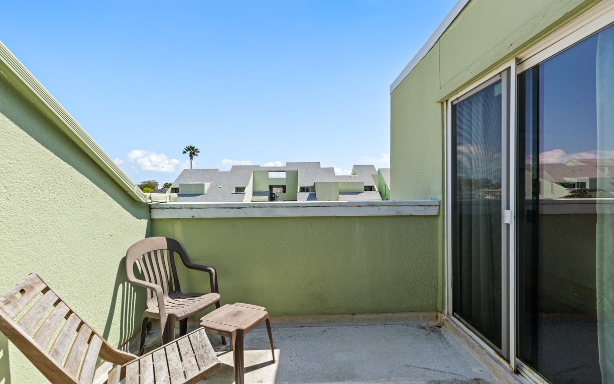 Step onto your private balcony for peaceful moments with outdoor seating and blue sky views above green rooftops.