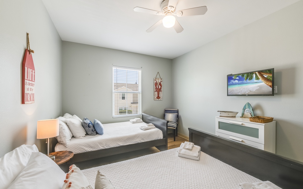 Unwind in your bright beach-themed bedroom with twin beds, coastal décor, and a relaxing ceiling fan for perfect comfort.