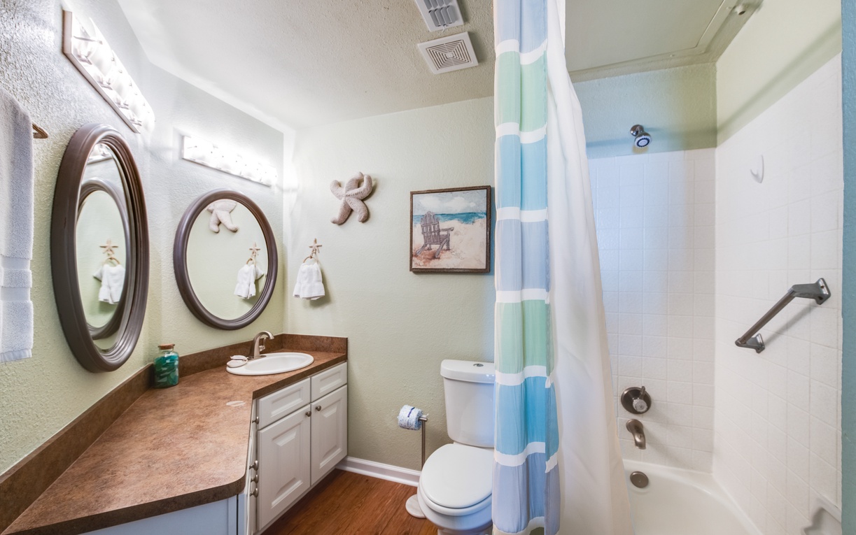 Refresh in your coastal-themed bathroom featuring dual vanities, a relaxing tub-shower combo, and charming beach-inspired touches.