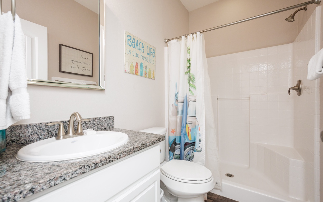 Step into your bright, coastal-themed bathroom with granite countertops and refreshing shower after beach adventures.
