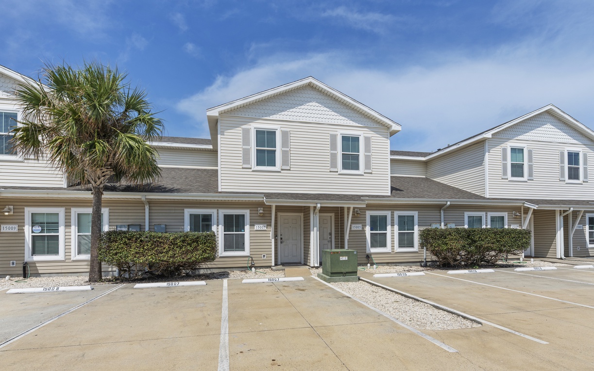 Modern townhome exterior featuring coastal-style architecture with convenient parking and tropical landscaping in a well-maintained community setting.