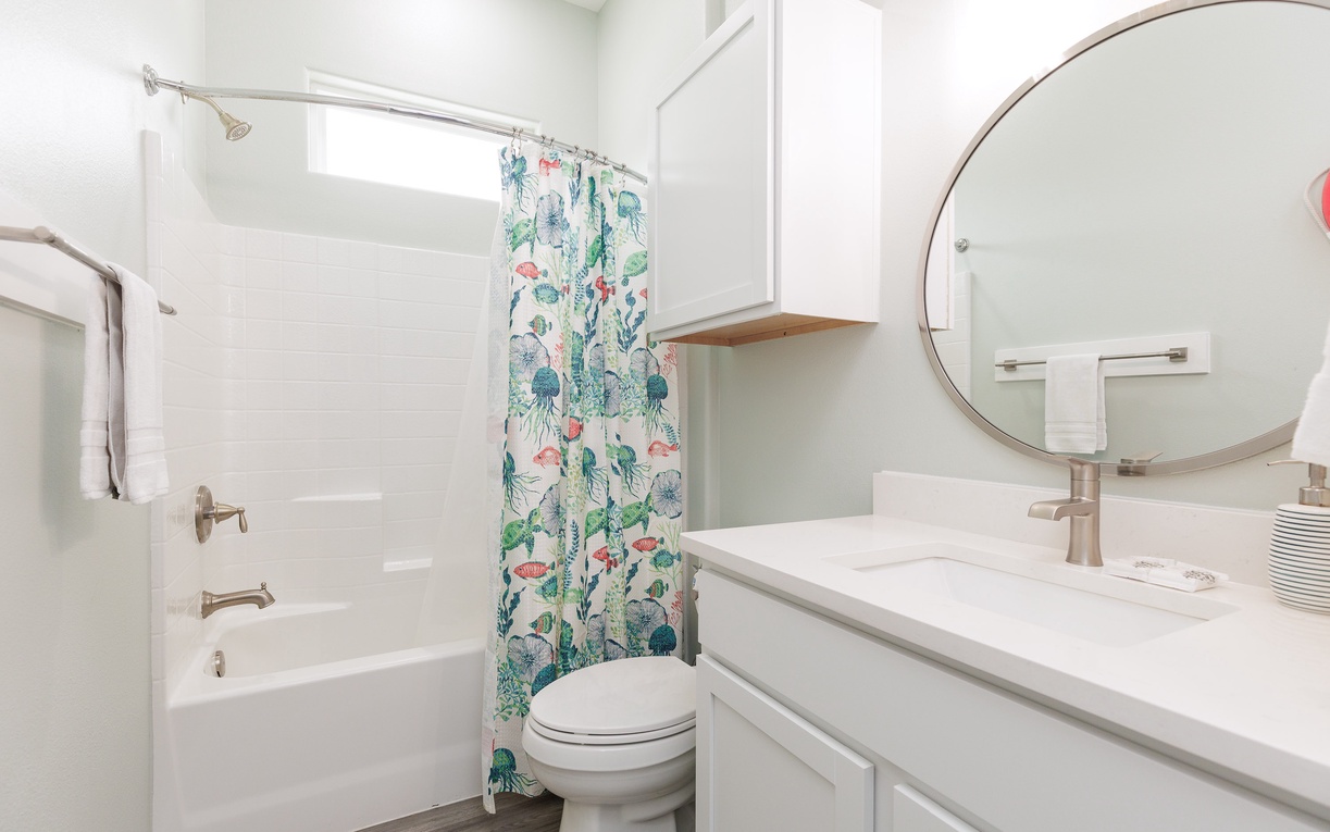 Refresh in your bright bathroom featuring a tropical-themed shower curtain, marble countertop, and modern amenities for your comfort.