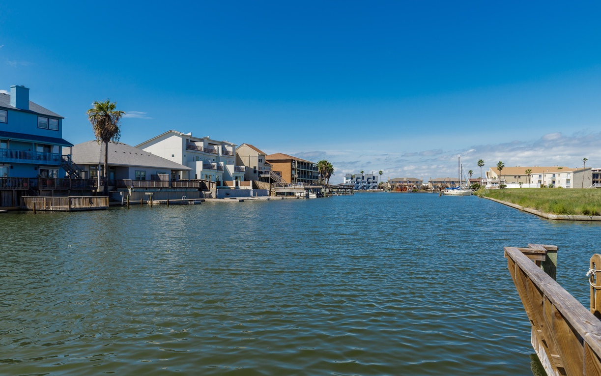 Waterfront canal community with colorful homes, palm trees, and marina under sunny blue skies near the property.