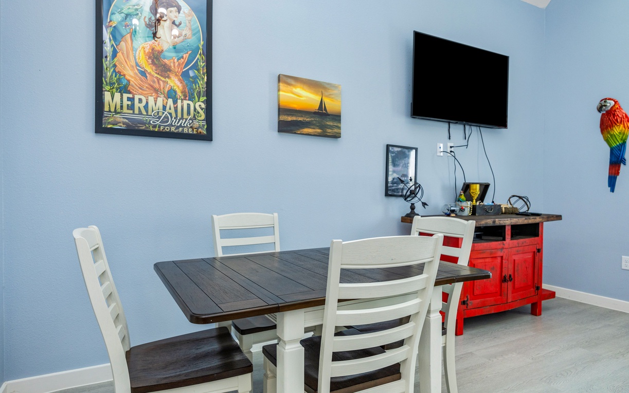 Gather around your charming dining table for meals while enjoying colorful coastal artwork and convenient entertainment on the wall-mounted TV.