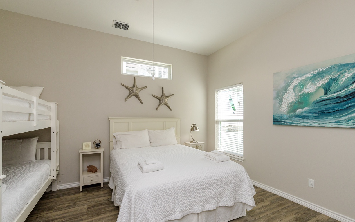 Rest peacefully in your coastal-themed bedroom with crisp white linens and ocean artwork creating a serene seaside atmosphere.