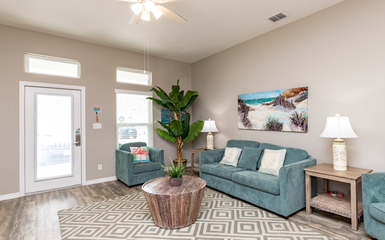 Relax in your coastal-themed living room with plush teal seating, tropical touches, and beachy artwork creating the perfect vacation vibe.