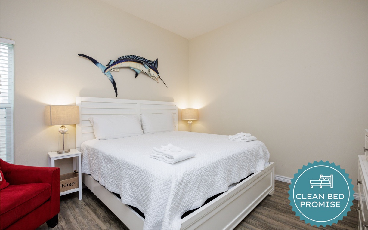 Rest peacefully in your nautical-themed bedroom with crisp white linens, cozy red seating, and warm bedside lighting.