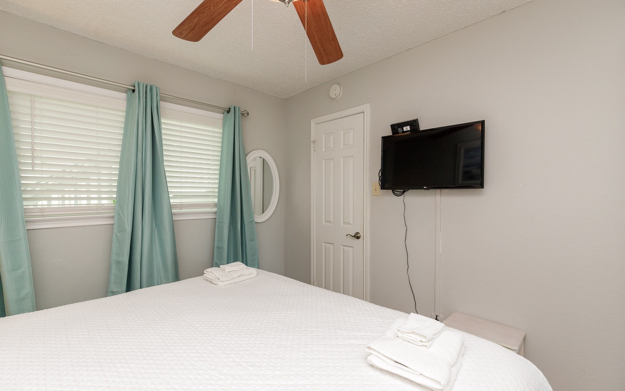 Relax in your peaceful bedroom with a ceiling fan, wall-mounted TV, and crisp linens ready for a restful night.