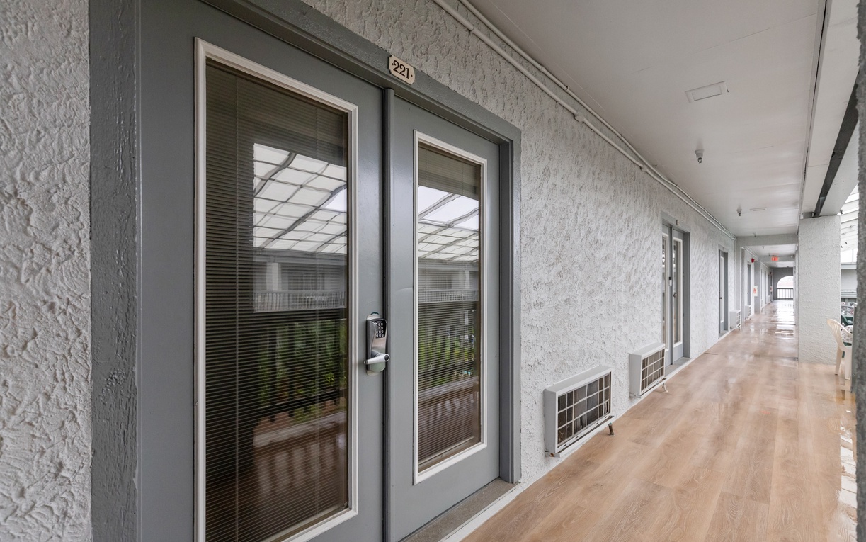 Bright corridors with numbered rooms lead you to comfortable accommodations, each featuring modern gray doors and natural light from skylights above.