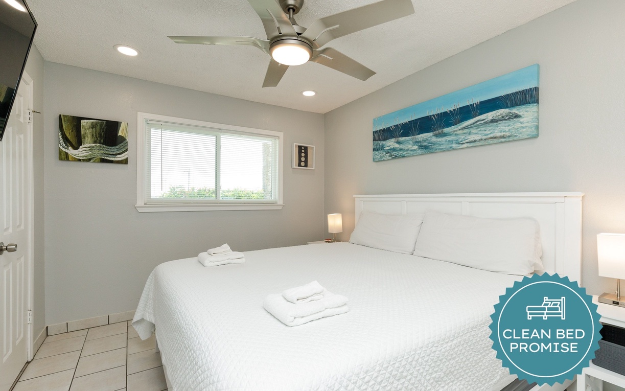 Drift into peaceful sleep in your bright, airy bedroom featuring crisp linens, ocean artwork, and cooling ceiling fan.