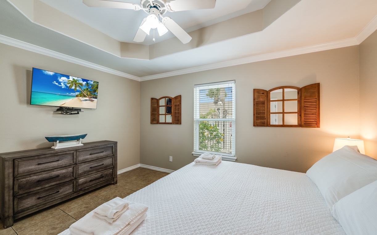 Unwind in your serene bedroom featuring a plush bed, entertainment center, and charming shuttered windows that let in gentle natural light.
