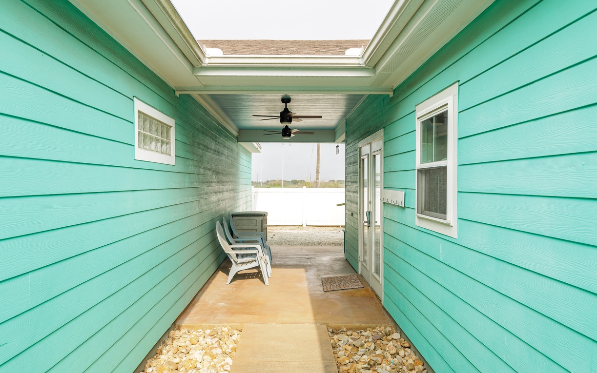 Step into your bright turquoise breezeway where coastal charm meets comfort. Relax in white chairs while ocean breezes flow through your covered entrance.