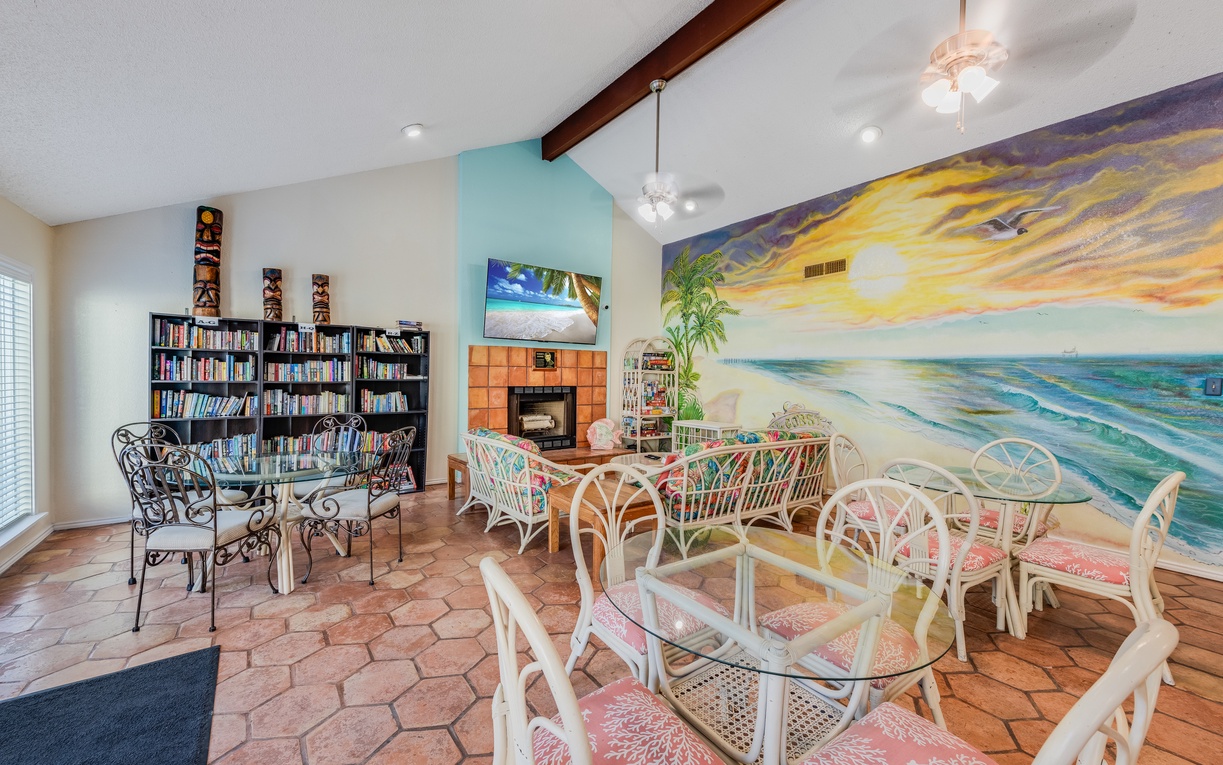 Relax in this vibrant communal space featuring comfortable seating, extensive book collection, and stunning ocean mural creating a peaceful beachside atmosphere.
