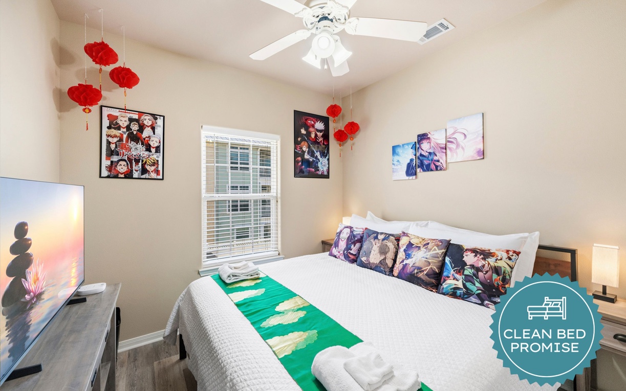 Sink into plush bedding under the soft glow of the ceiling fan in your cozy bedroom, where vibrant art and serene lighting create a welcoming, personalized retreat just for you.