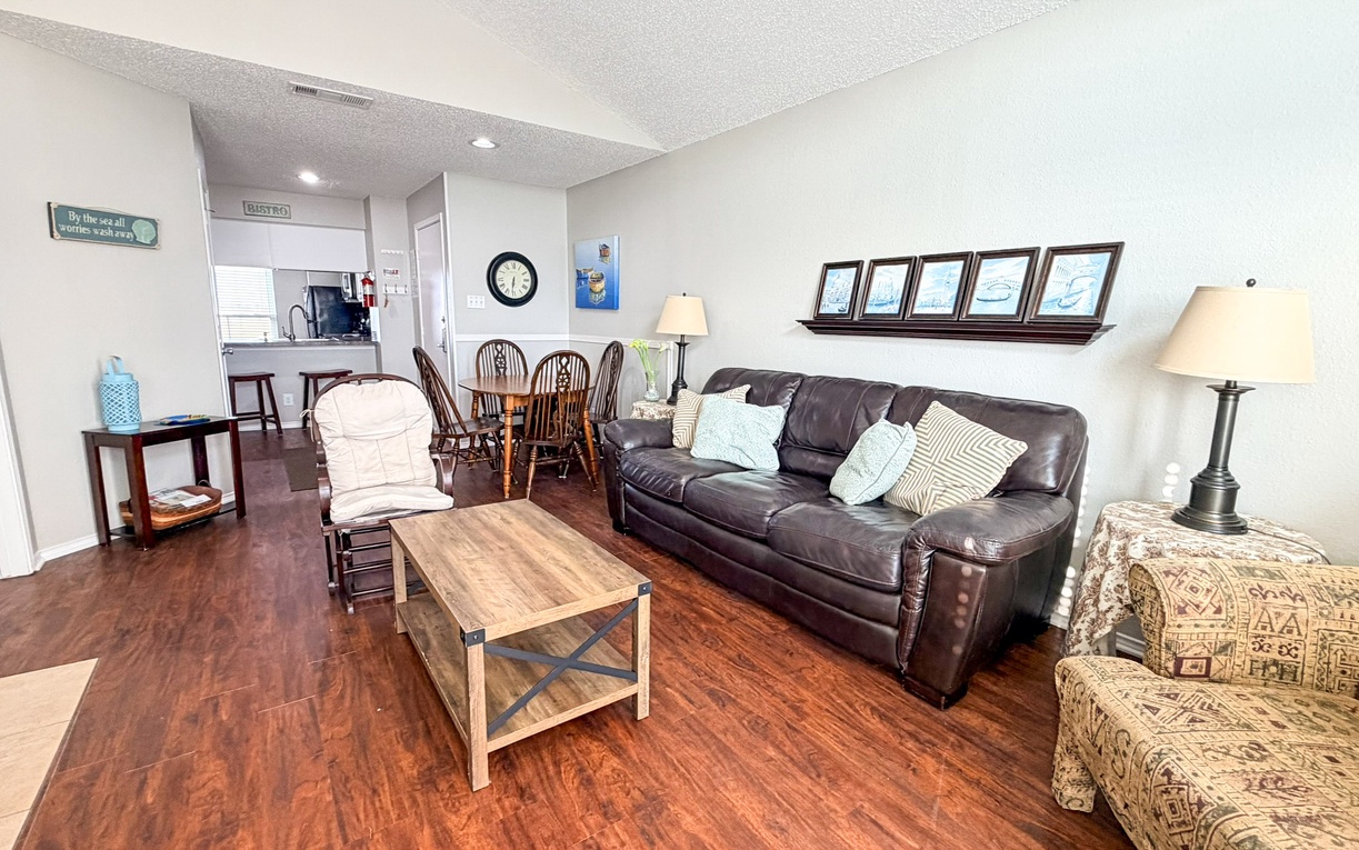 Relax in your spacious living area with comfortable leather seating, warm wood floors, and coastal artwork creating the perfect retreat atmosphere.