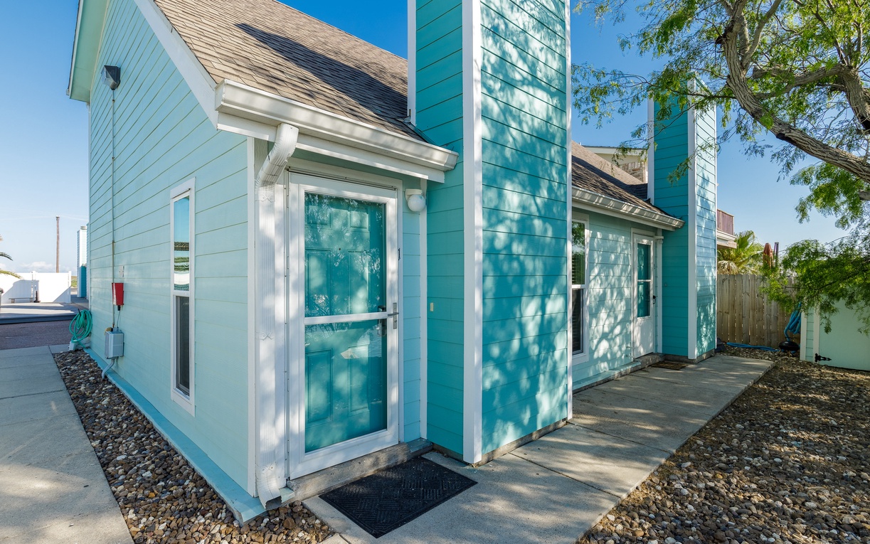 Charming turquoise cottage featuring a welcoming glass door entrance with modern architectural details and thoughtful landscaping in a peaceful setting.