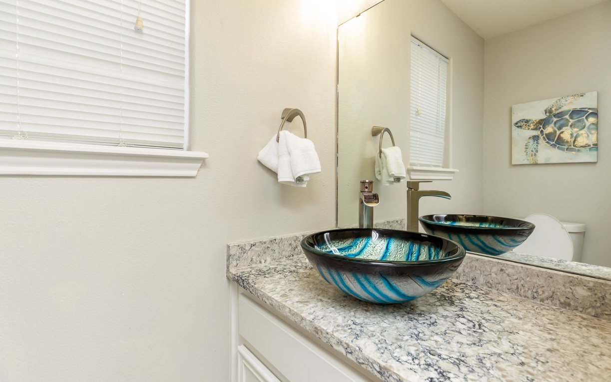 Refresh in your elegant bathroom featuring stunning glass vessel sinks with ocean-inspired blues and luxurious granite countertops.