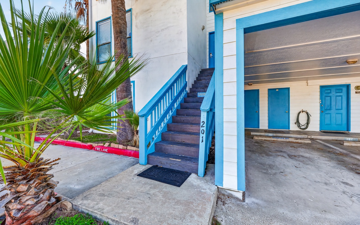 Bright coastal-inspired exteriors with turquoise accents welcome you to this beach retreat. Palm trees frame the building, hinting at the laid-back vibe that awaits.