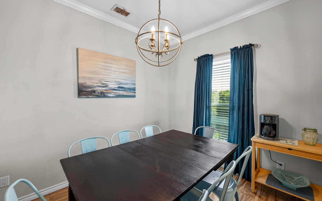 Gather your group around this welcoming dining table, where natural light streams through the windows and coastal artwork sets a relaxed, beachy tone for shared meals and conversation.
