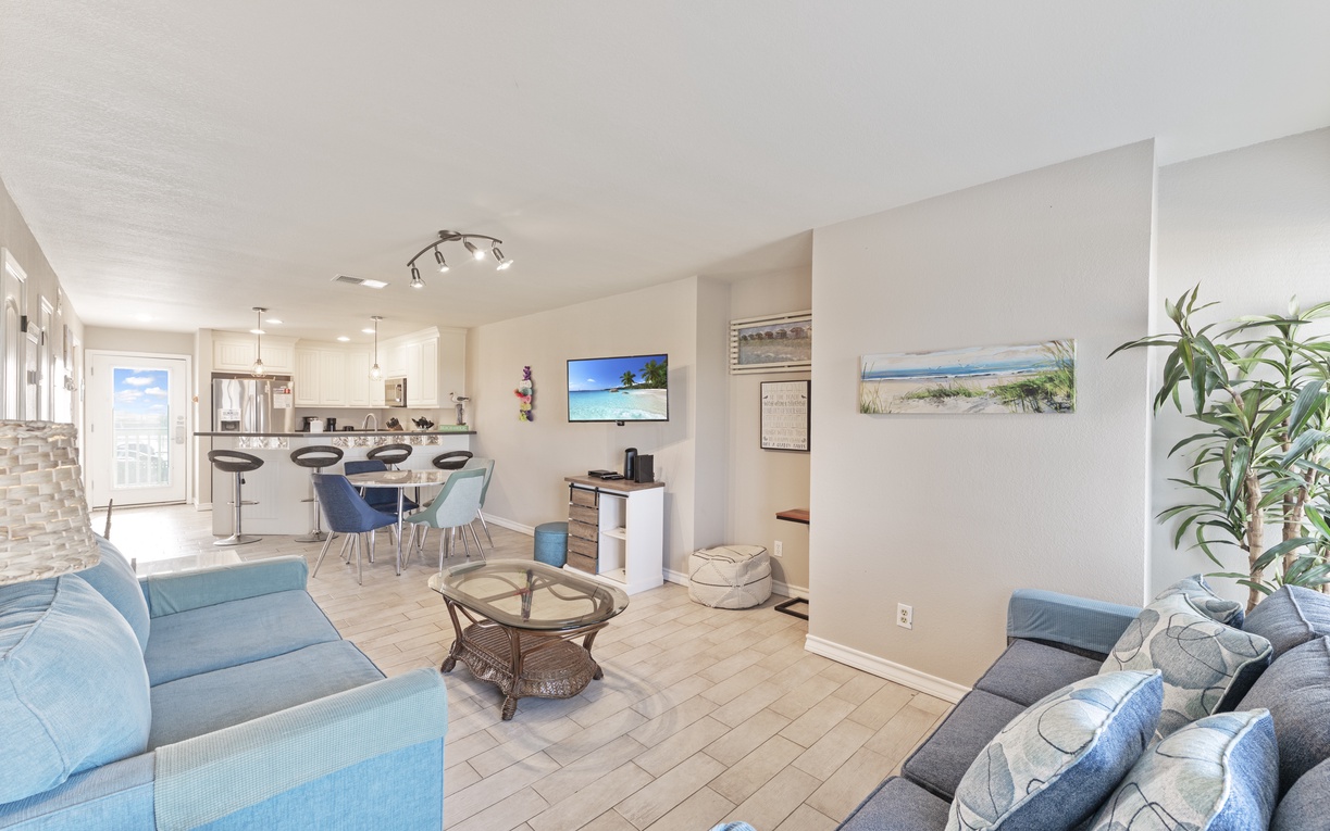 Relax in your bright open-concept space where coastal blue furnishings meet modern comfort, creating the perfect beach retreat atmosphere.