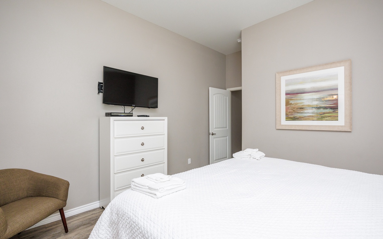 Unwind in your peaceful bedroom with plush linens, modern TV, and cozy seating for ultimate relaxation.