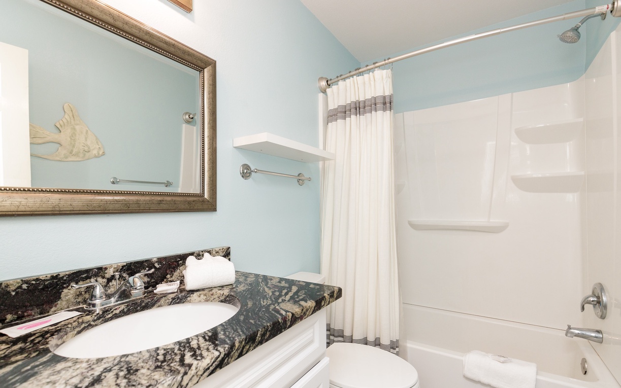 Refresh in your private second floor guest bathroom featuring elegant granite countertops, soothing blue walls, and a spacious tub-shower combo for ultimate relaxation.