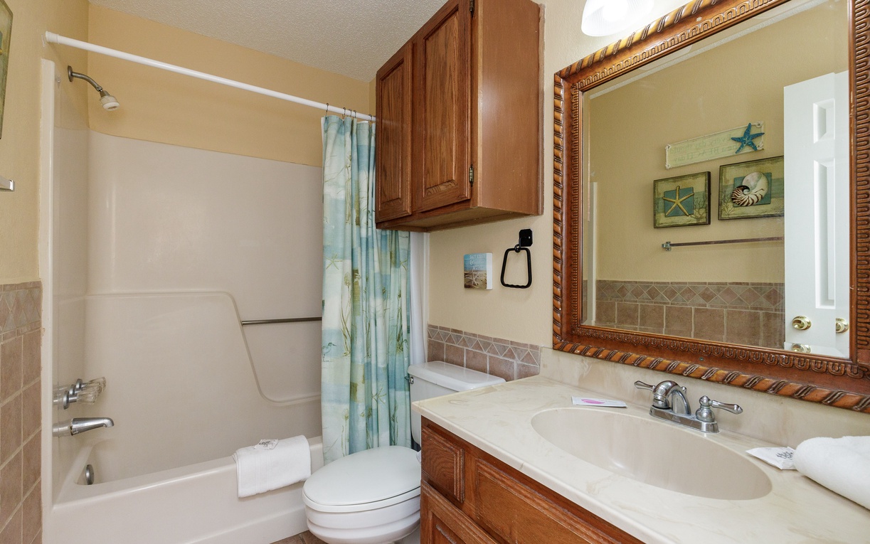 Refresh in your coastal-themed bathroom featuring warm wood cabinetry, tiled accents, and charming seaside decor that creates a peaceful retreat.
