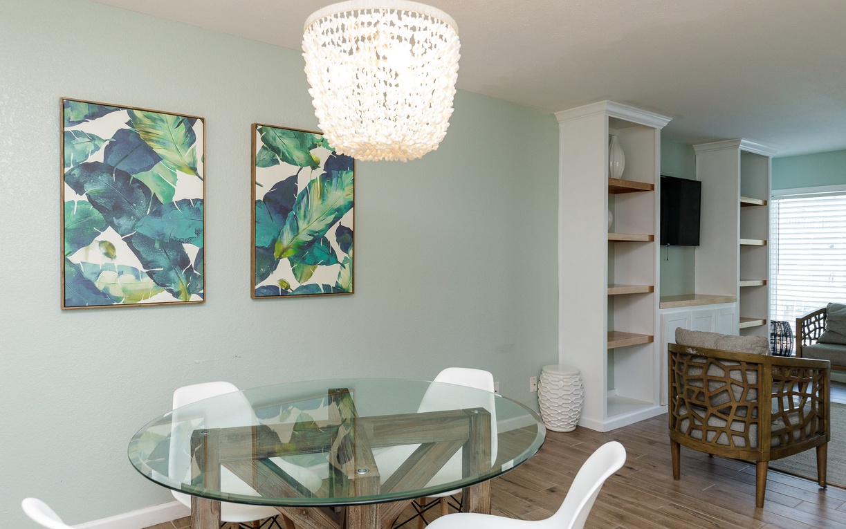 Dine in style beneath your stunning chandelier at this elegant glass table, surrounded by coastal-inspired decor.