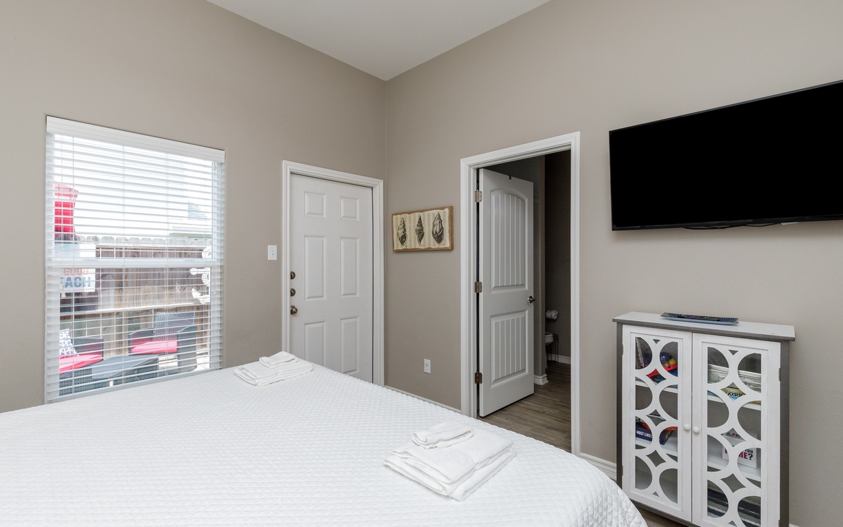 Unwind in your cozy bedroom featuring a comfortable bed, smart TV entertainment, and bright windows bringing in natural light.