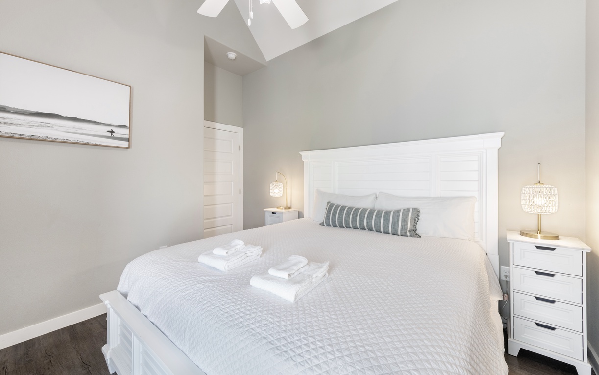 Sink into your plush bed beneath soaring ceilings and gentle natural light, where coastal artwork and fluffy towels await your peaceful retreat.