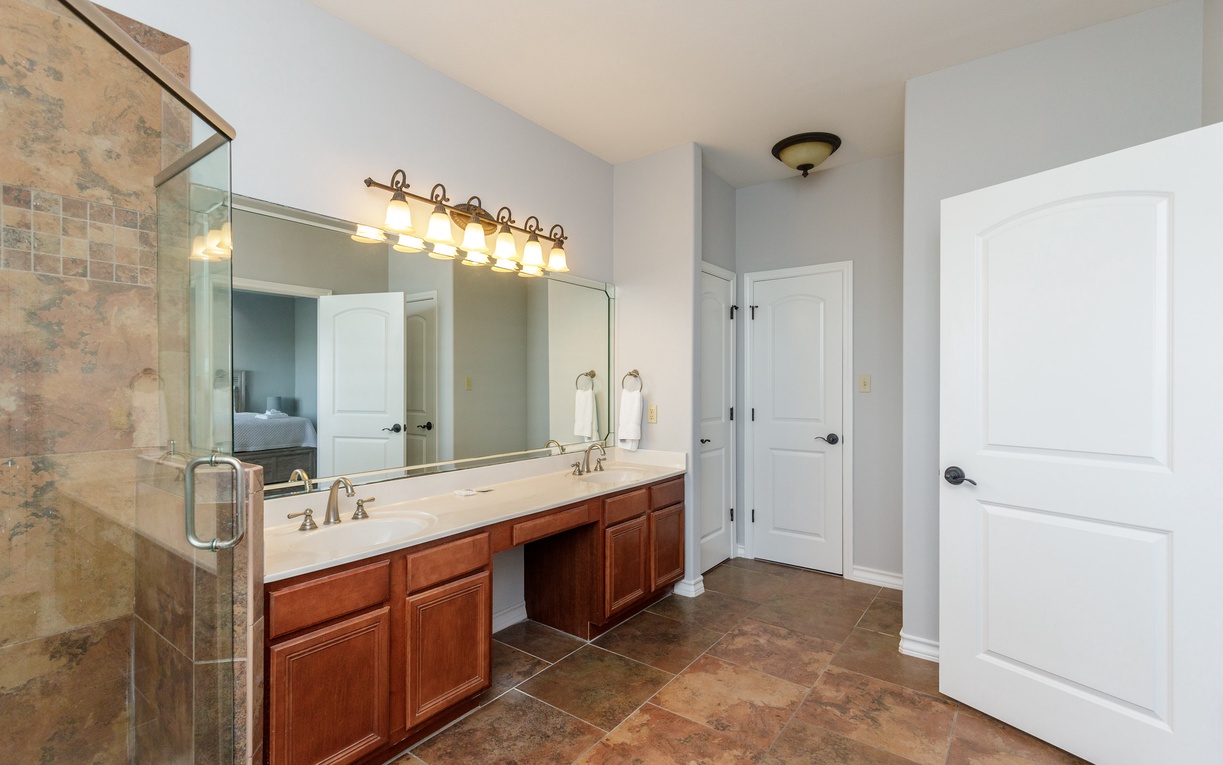 Prepare for your day in this spacious master bathroom featuring elegant dual vanities, abundant storage, and beautiful natural stone finishes.