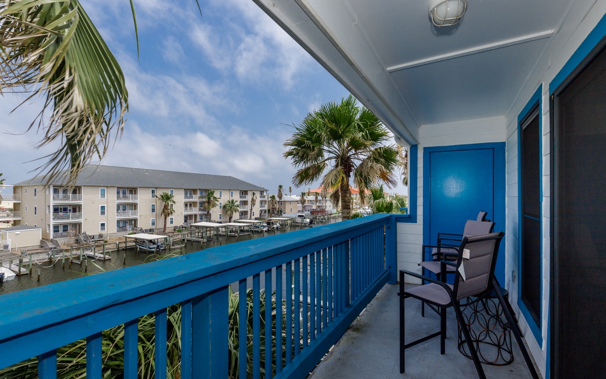 Waterfront views from your private balcony feature marina boats, palm trees, and neighboring coastal buildings under tropical blue skies.