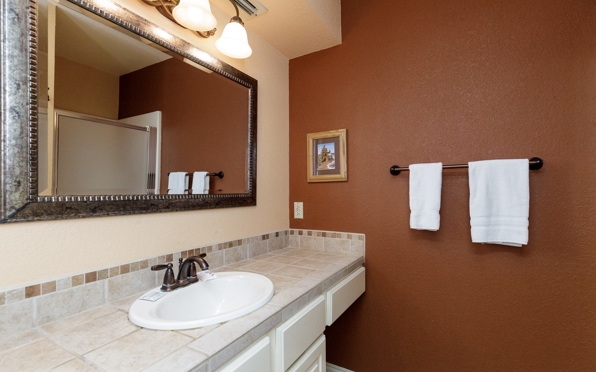 Freshen up in this elegantly appointed bathroom featuring warm earth tones, decorative mirror, and pristine white towels for your comfort.