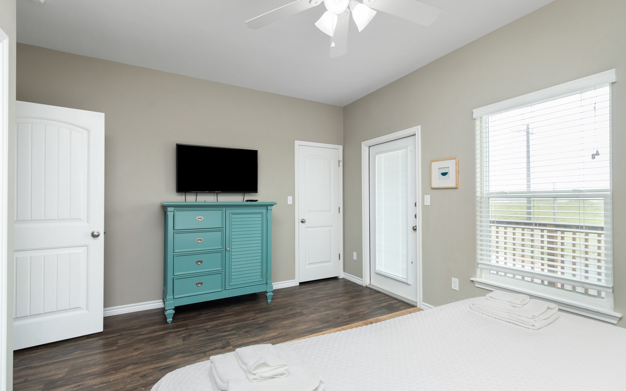 Relax in your bright bedroom with wall-mounted TV, charming turquoise dresser, and ceiling fan for perfect temperature control.