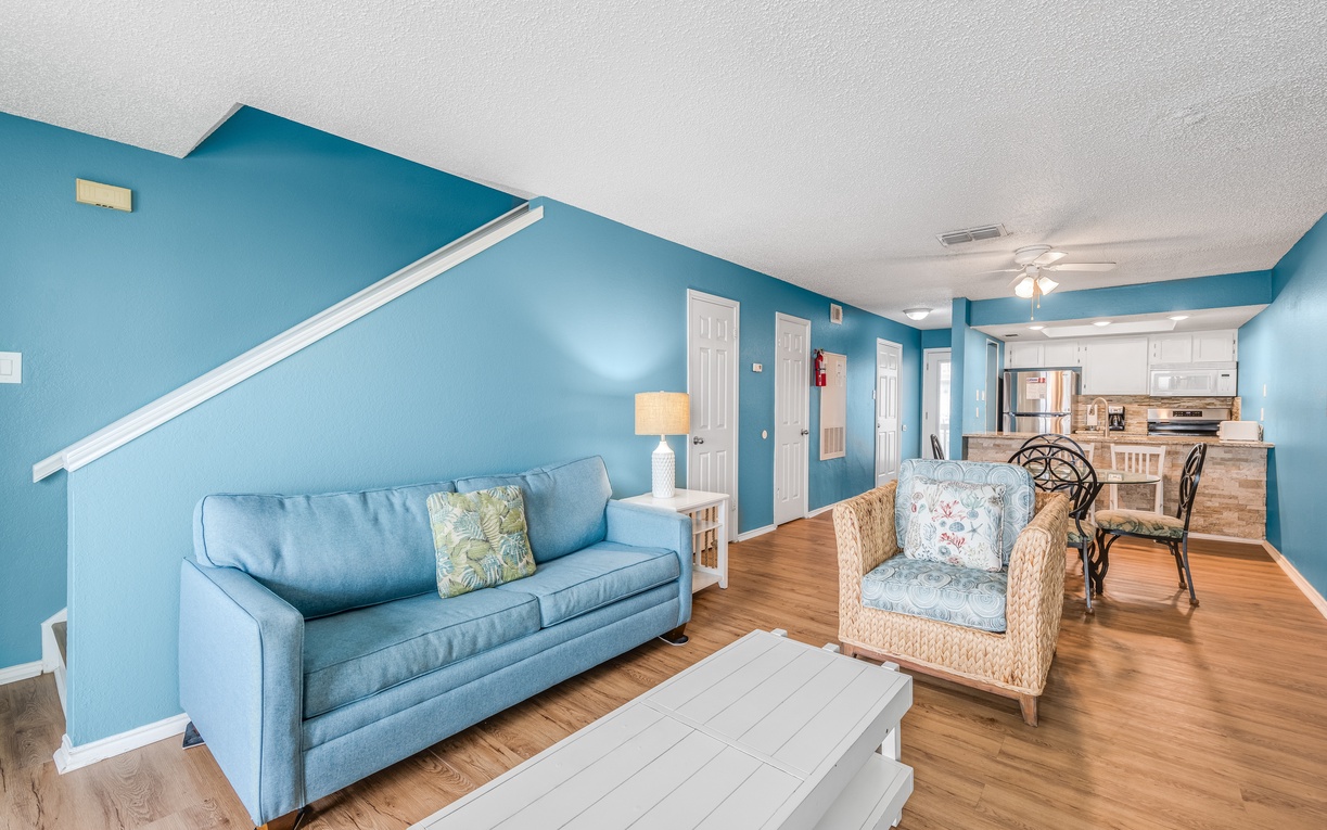 Relax in your spacious open-plan living area with coastal blue walls, comfortable seating, and a fully equipped kitchen.