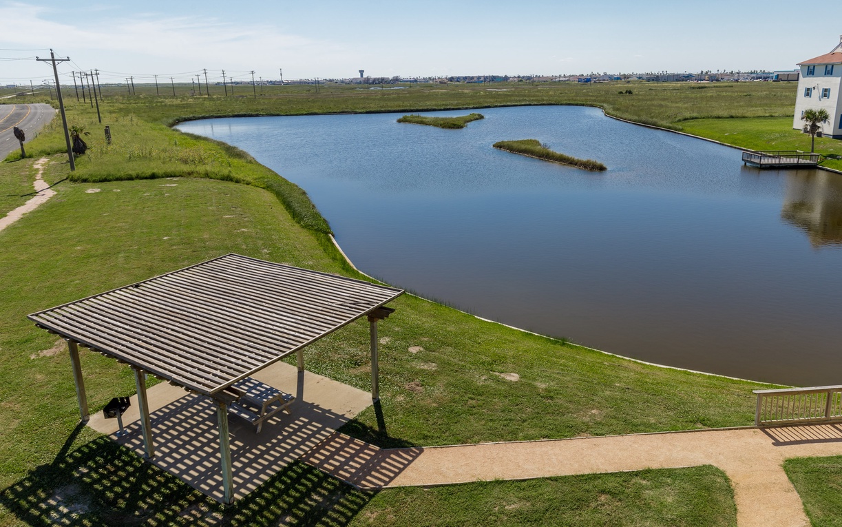 Aerial view captures the peaceful lakeside setting with covered picnic area and walking paths surrounding this tranquil water feature.