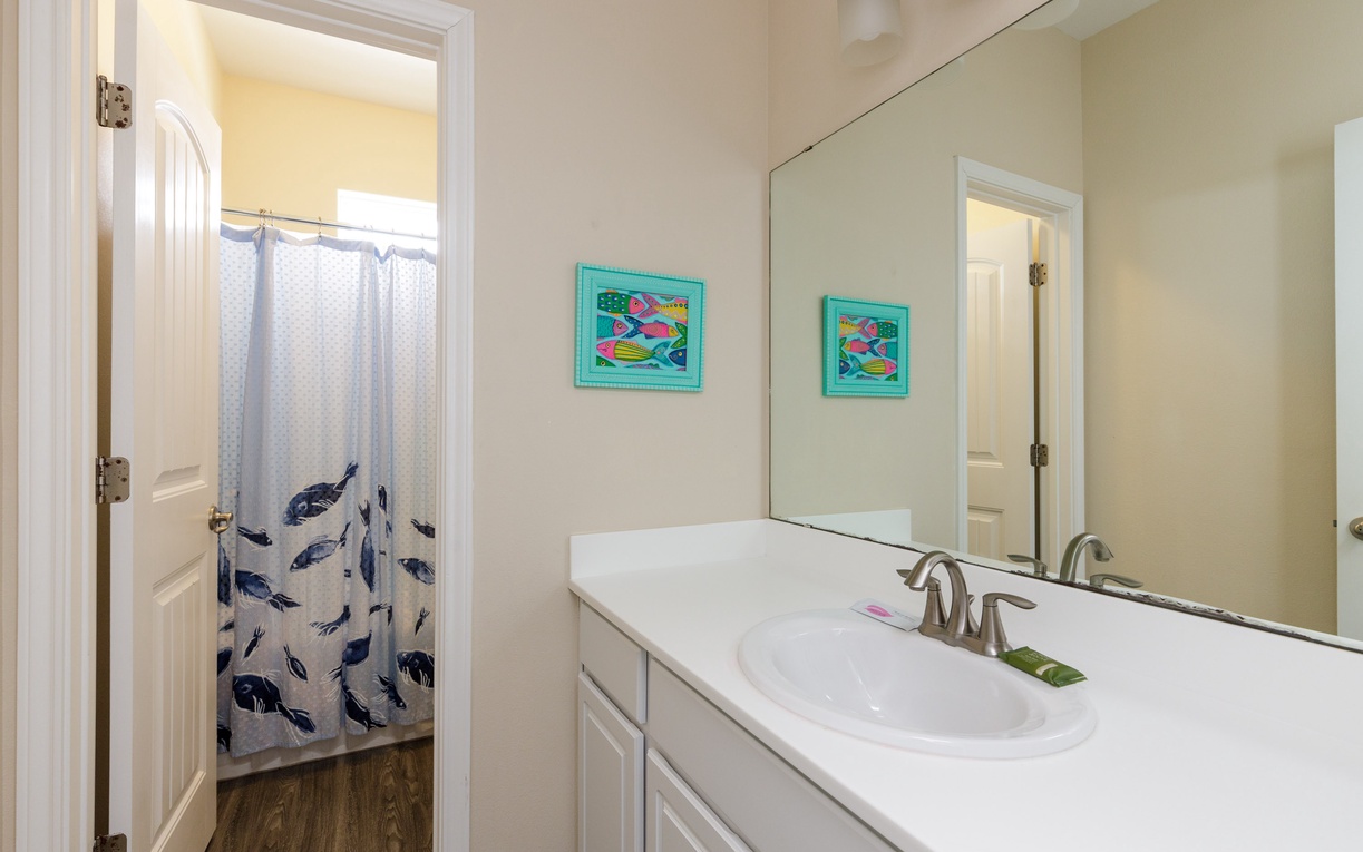 Your private bathroom features a clean vanity and whimsical fish-themed shower curtain, creating a cheerful coastal vibe for your morning routine.