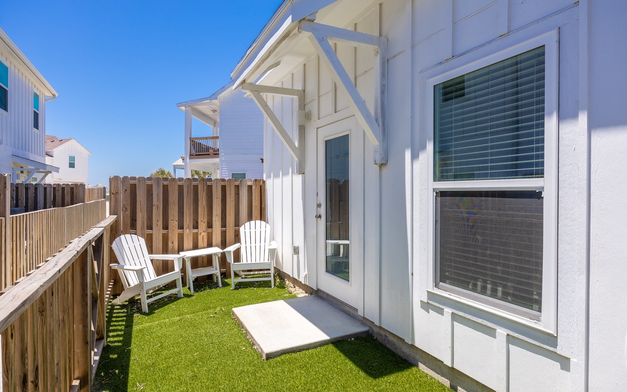 Relax in your private backyard oasis with comfortable Adirondack chairs and lush artificial turf for barefoot lounging.