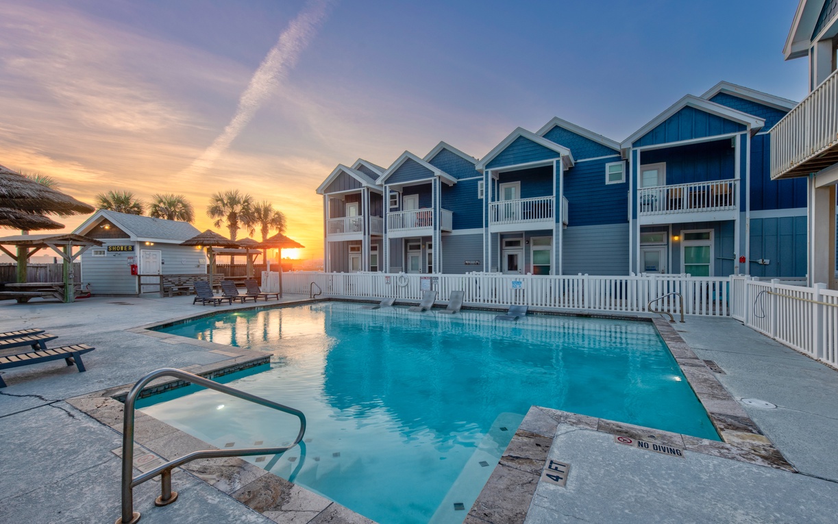 Colorful beachside resort featuring blue coastal cottages surrounding a sparkling pool during golden hour sunset.