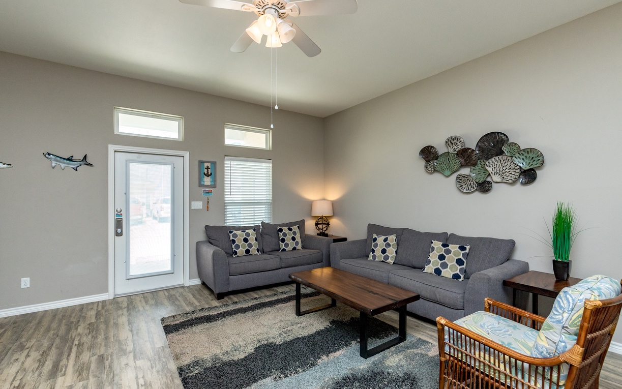 Unwind in your spacious living room with comfortable seating, modern coastal decor, and natural light streaming through multiple windows.