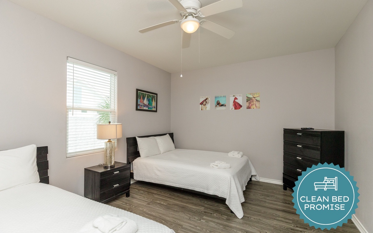 Relax in your bright, comfortable bedroom with two cozy beds, ceiling fan, and cheerful wall art creating the perfect space to unwind.