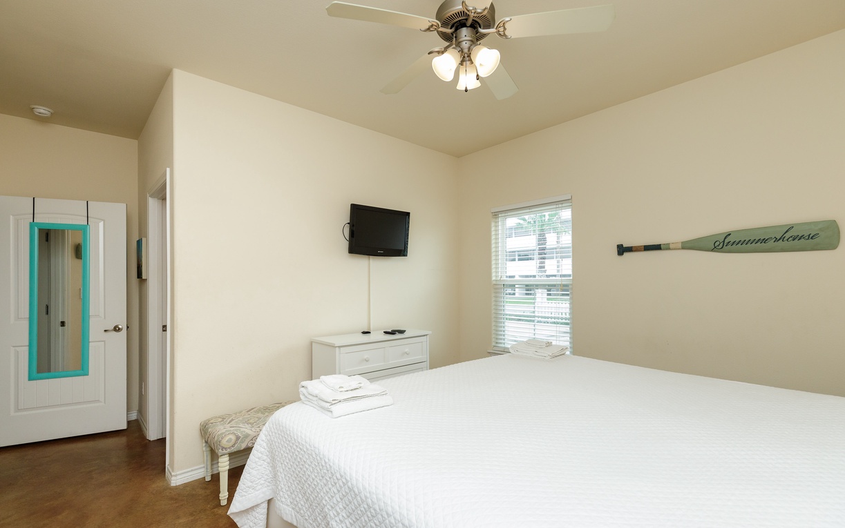 Relax in your bright bedroom with coastal charm, complete with ceiling fan and wall-mounted TV for your comfort.