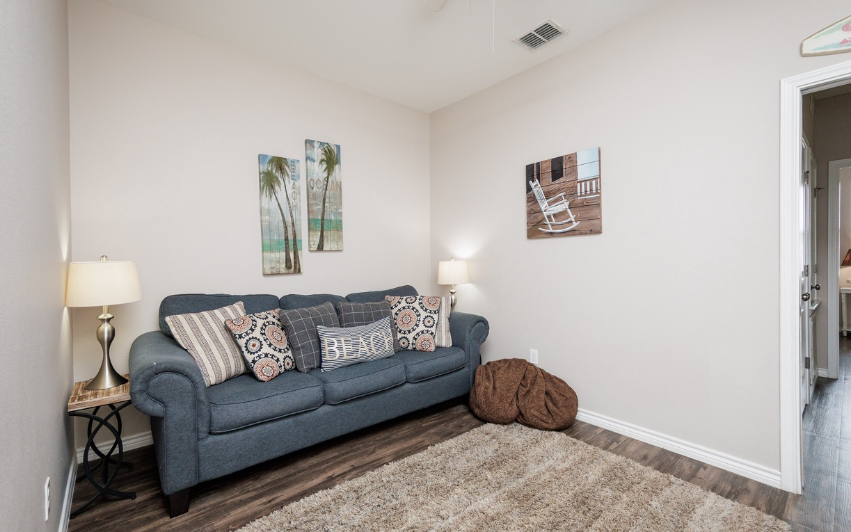 Unwind on the plush sofa with coastal artwork, soft throws, and warm lighting creating your perfect reading nook.