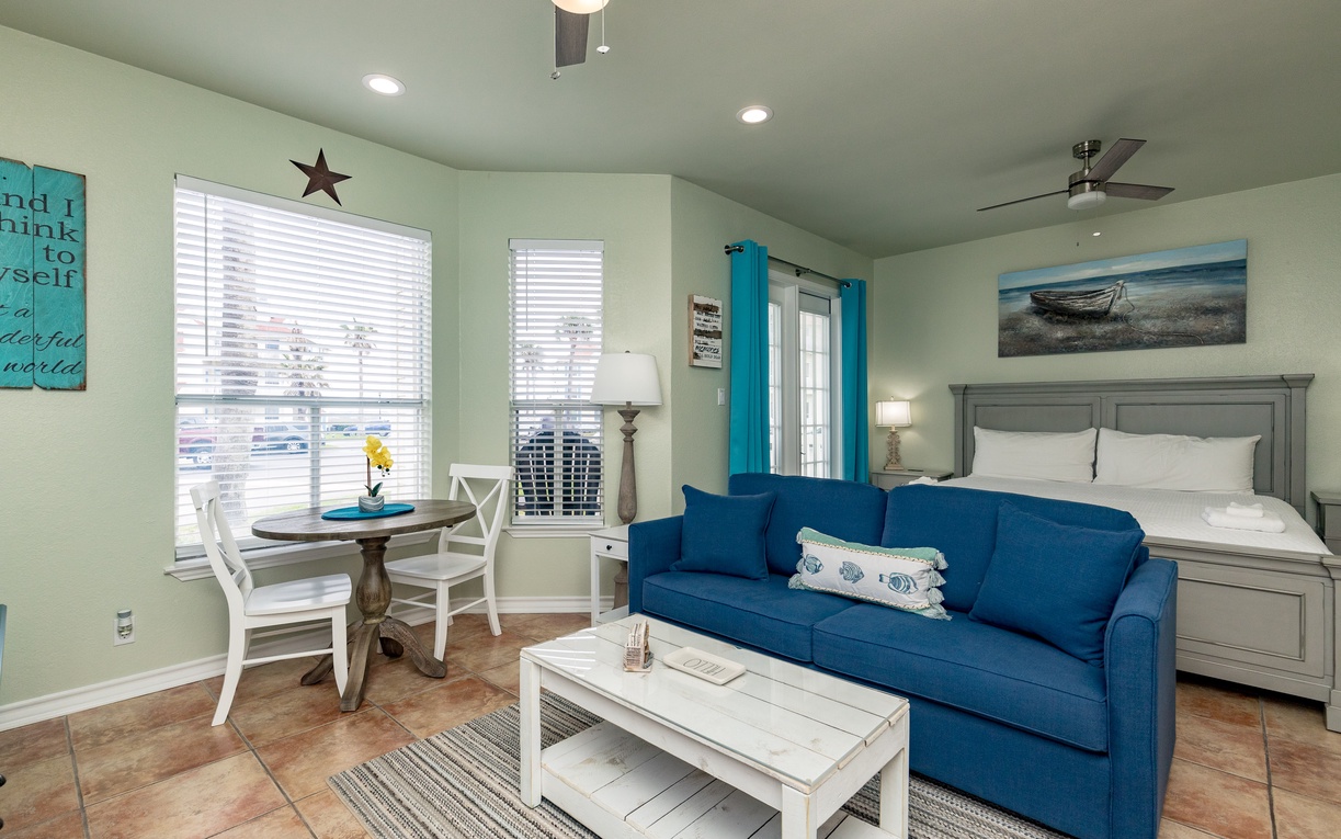 Relax in your coastal-themed studio with comfortable seating, dining space, and peaceful ocean artwork creating the perfect beach getaway atmosphere.