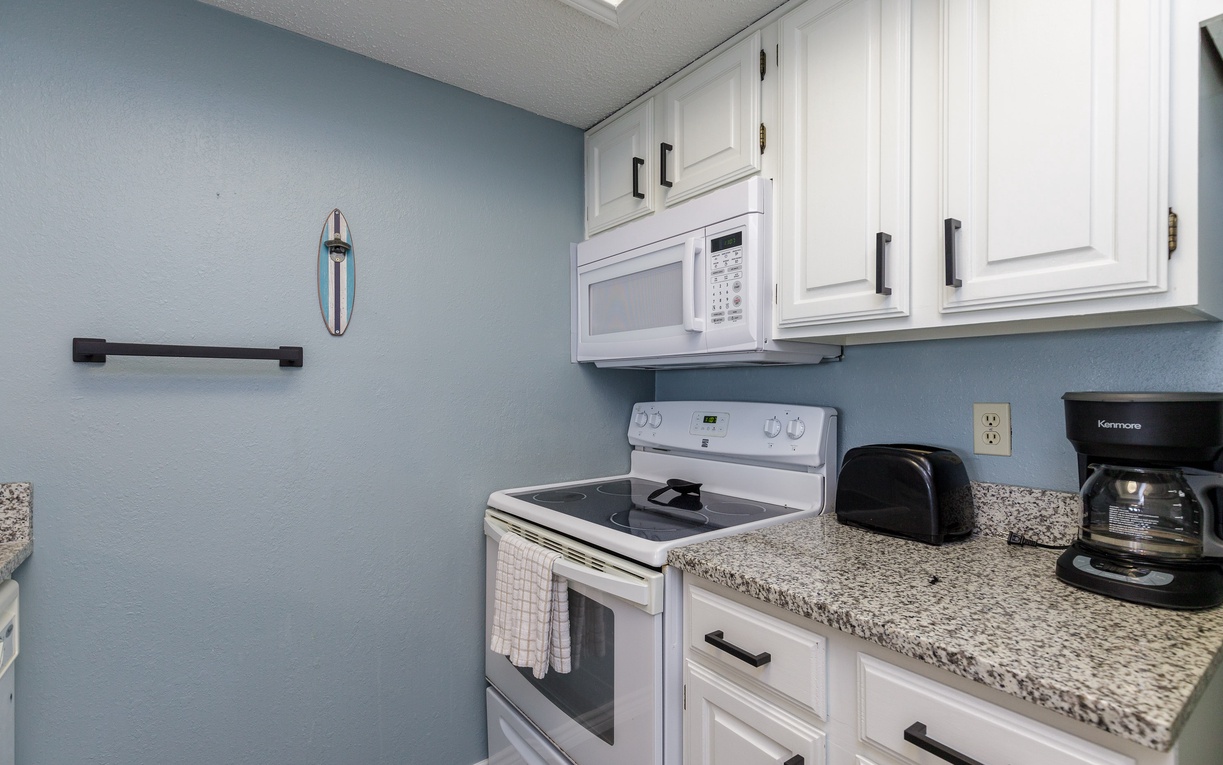Your fully equipped kitchen features granite countertops, white appliances, and soothing blue walls. Everything you need for home-cooked meals during your stay.