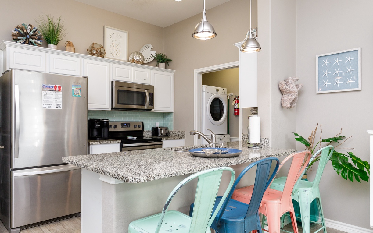Your bright kitchen features granite counters, stainless appliances, and colorful coastal stools perfect for morning coffee or meal prep.