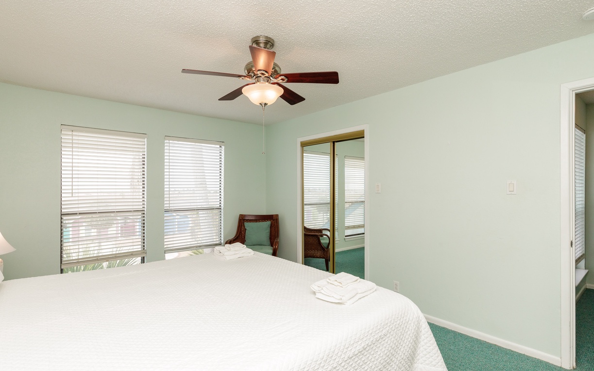 Your peaceful bedroom features soft green walls, a ceiling fan for comfort, and fresh linens waiting for your arrival.